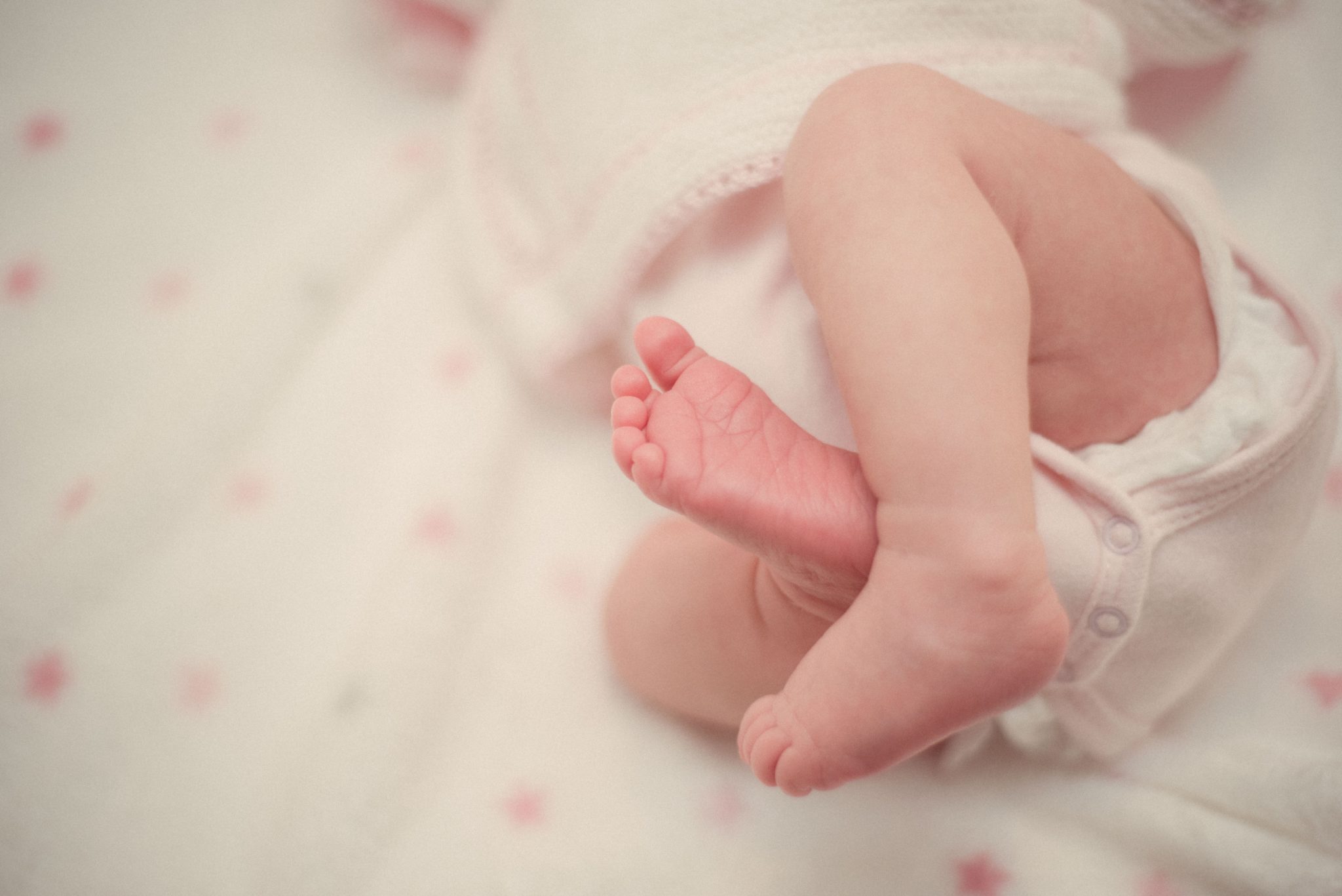 Close up image of an infant's legs lying on white bed sheets.