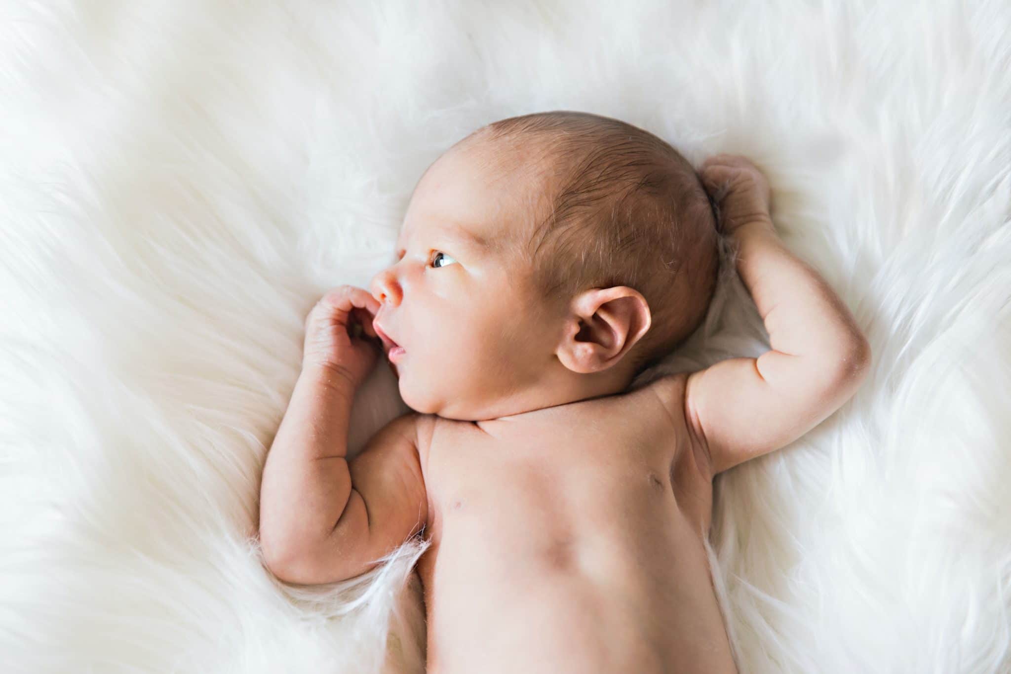 Infant lying on their backs on a white blanket.