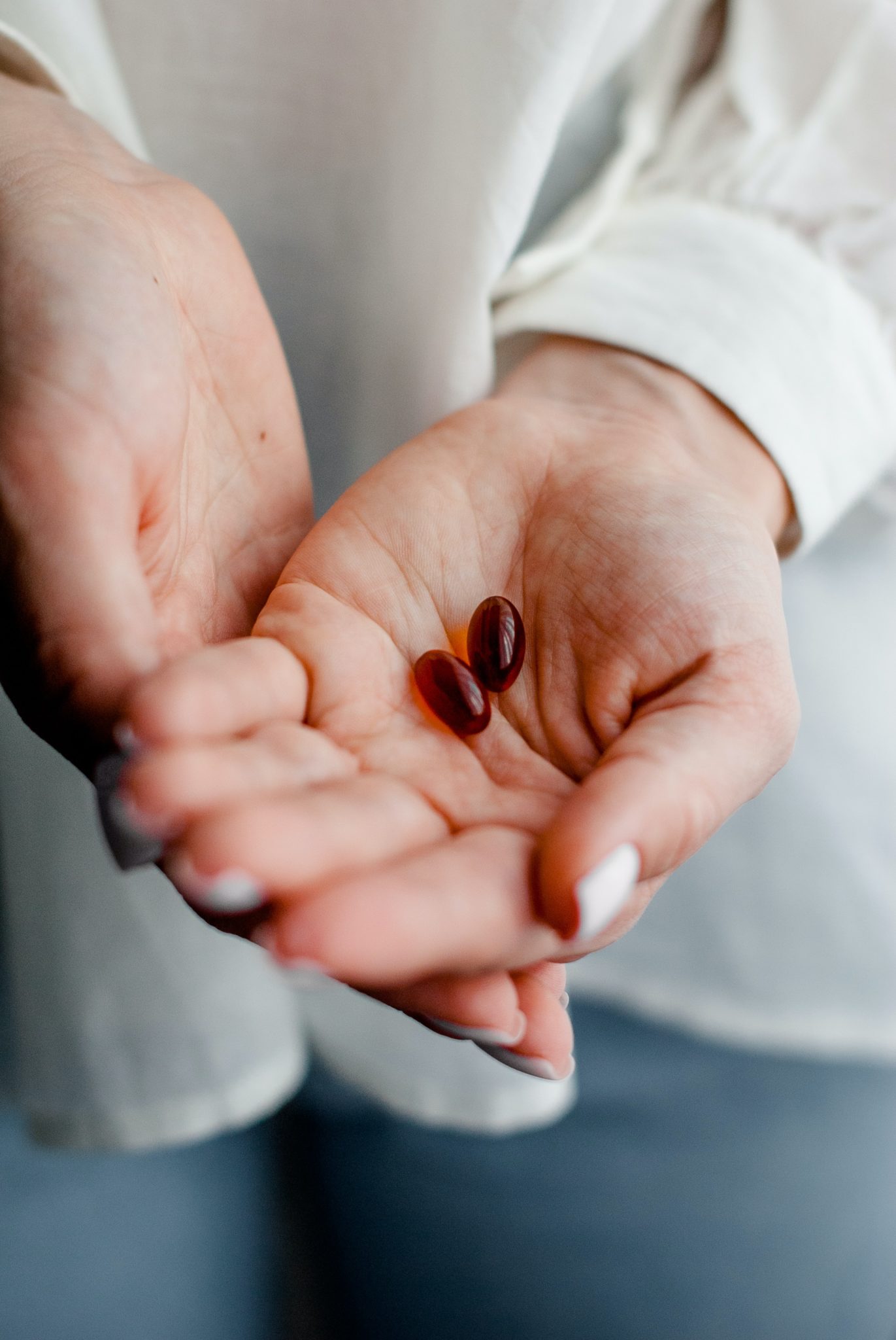 close up of two hands holding two small red pills 