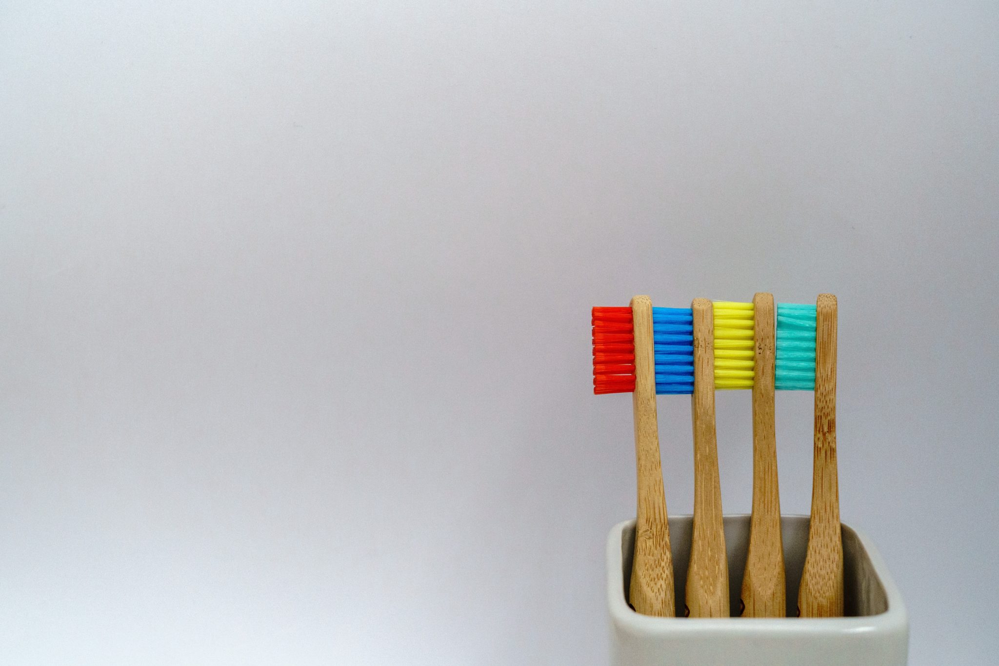 Multiple wooden toothbrushes for children lined up against each other against a white background.