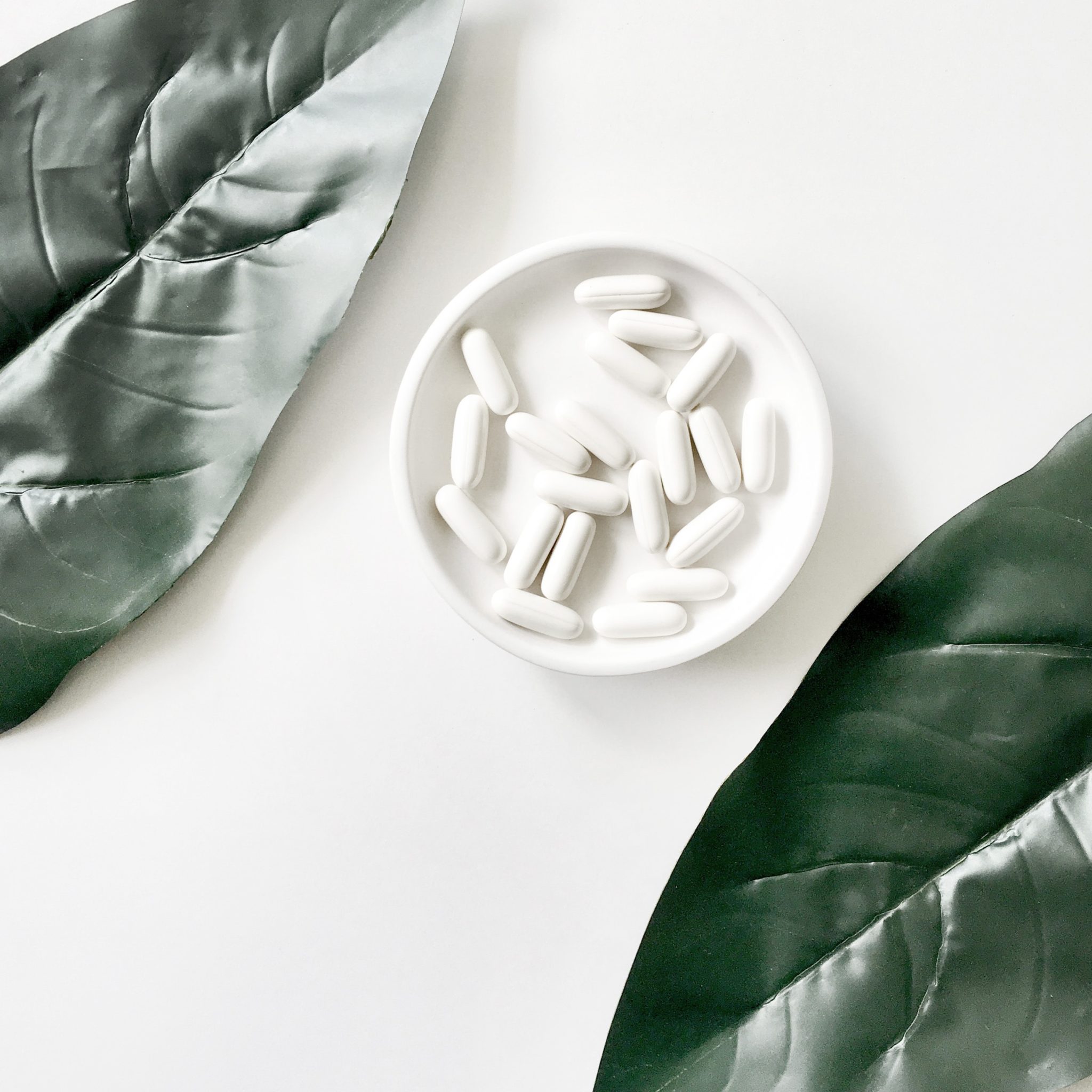 birds eye image of white fertility supplements in a white bowl against a white background with 2 green plants in the upper left and lower right corners