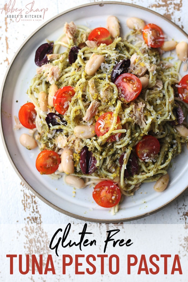 birds eye shot of gluten free tuna pesto pasta on a white plate garnished with olives, tomatoes, and parmesan cheese