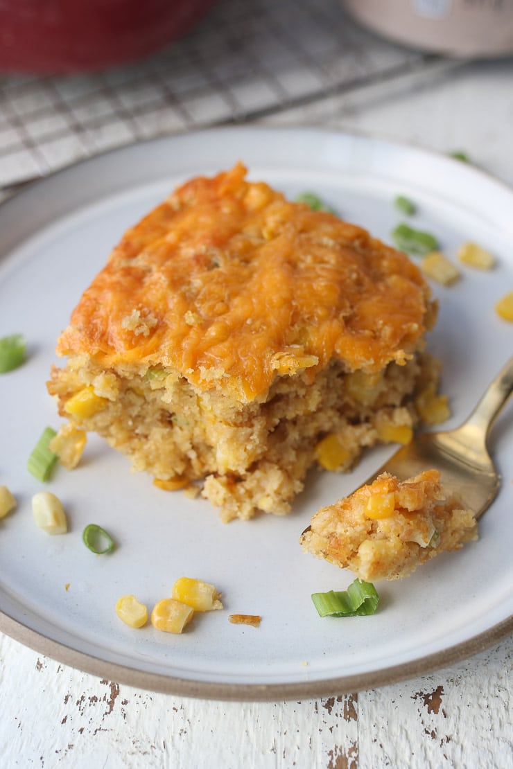 vegan corn spoonbread on a white plate garnished with corn and green onions 