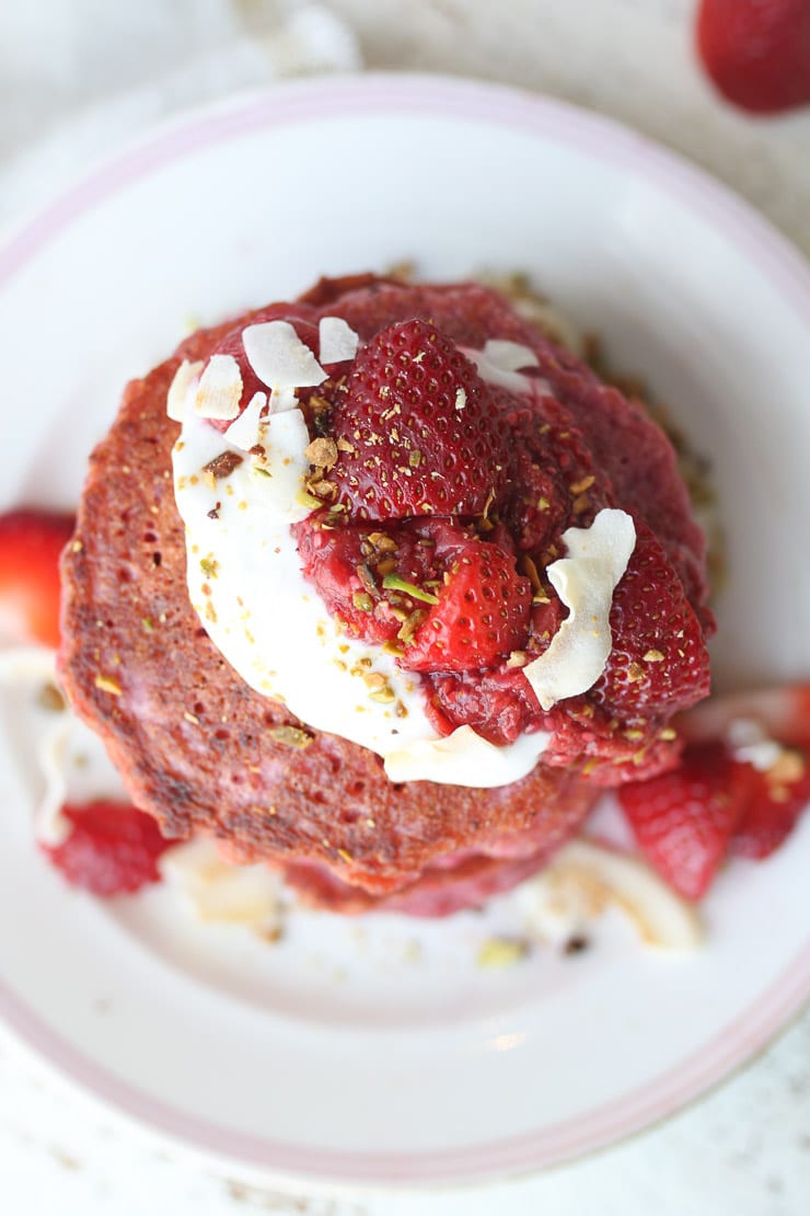 Birds eye view of pink vegan oatmeal pancakes topped with strawberries and yogurt.