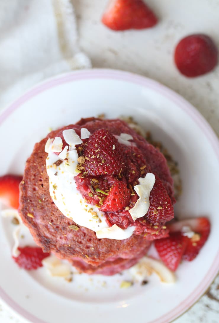 birds eye view of vegan pink oatmeal pancakes garnished with fresh berries and chopped nuts on a white plate