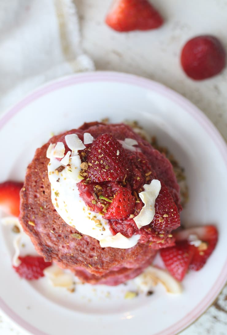 birds eye view of vegan pink oatmeal pancakes garnished with fresh berries and chopped nuts on a white plate 