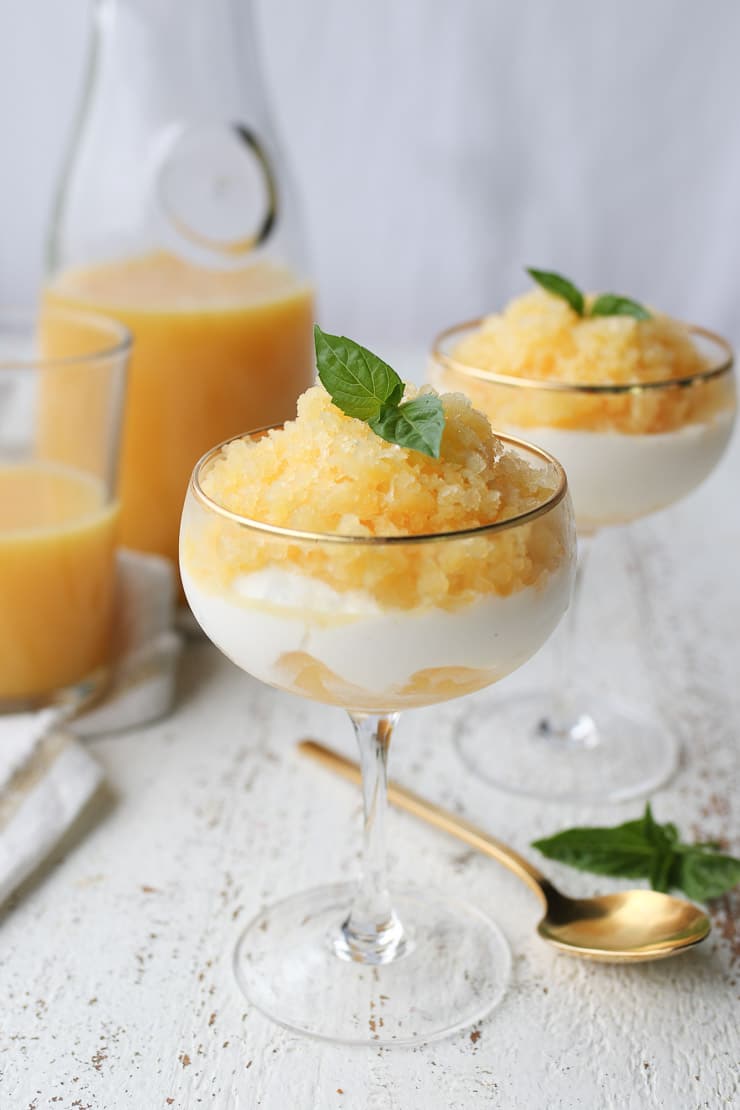 orange granita in to serving glasses topped with a basil leaf with Florida orange juice in the background 