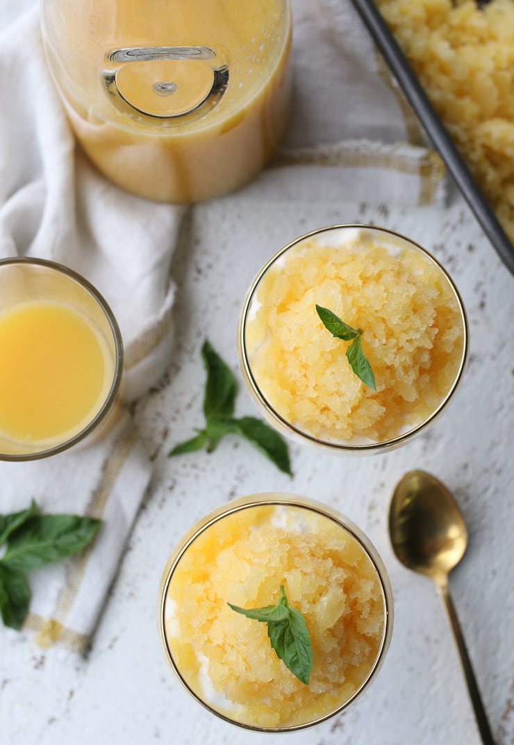 birds eye view of orange flavoured vegan granita parfait in two serving glasses topped with basil leaves 