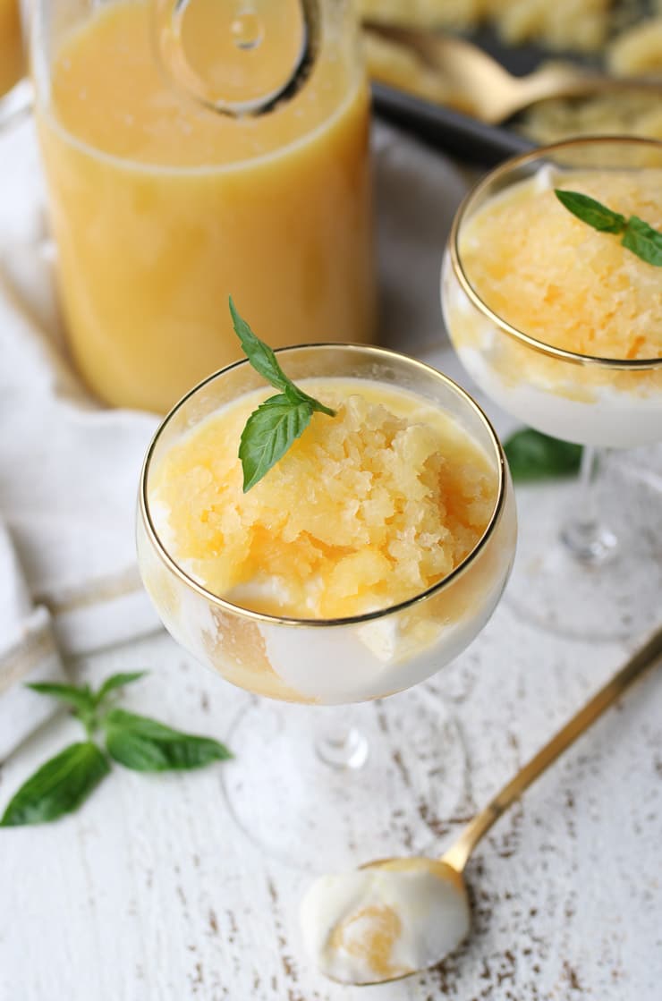 orange granita parfait in a serving glass topped with a basil leaf with Florida orange juice in the background 