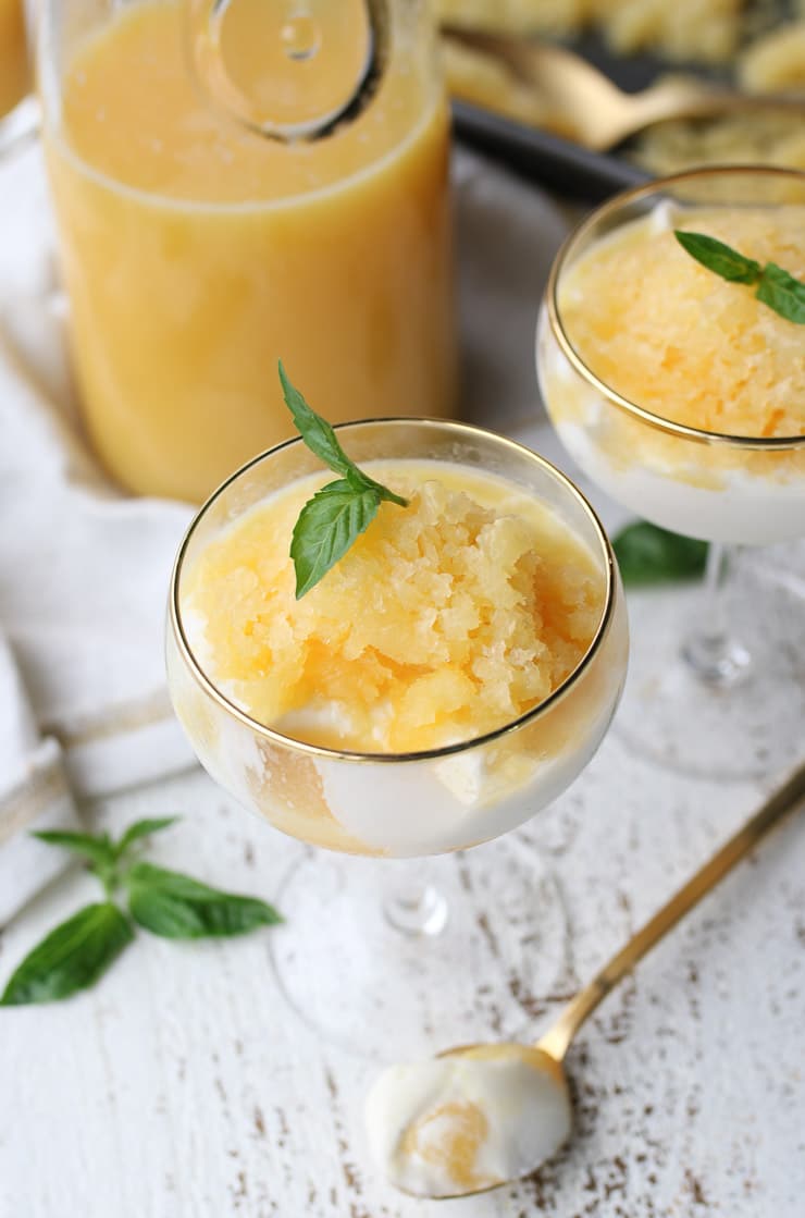orange granita parfait in a serving glass topped with a basil leaf with Florida orange juice in the background 