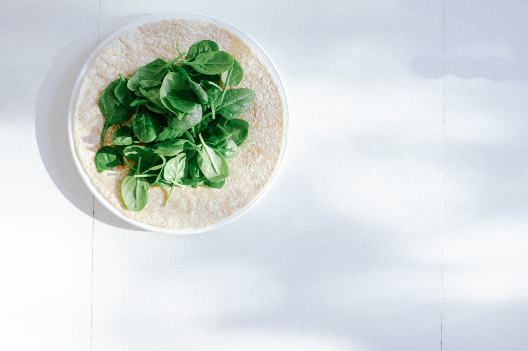 several leaves of spinach on top of a white tortilla to represent antinutrients like oxalates
