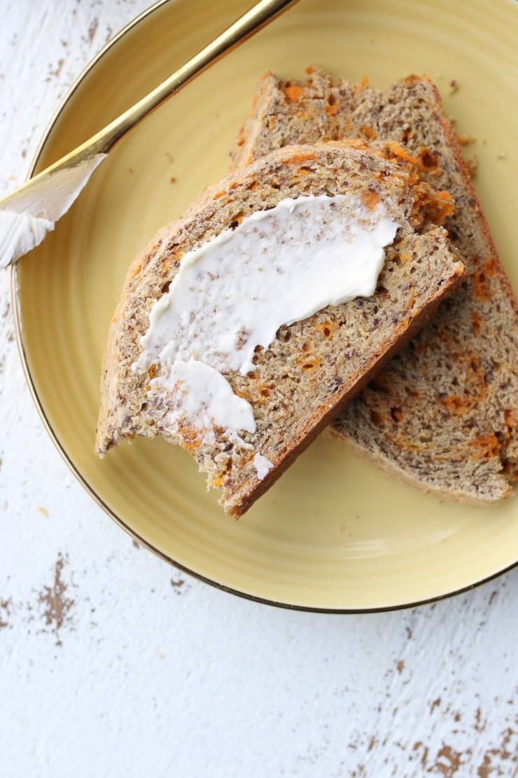 Two slices of soda bread on a yellow plate with butter spread on top with a gold butter knife.