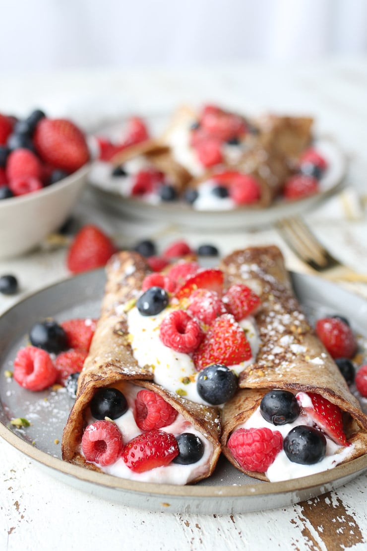 Two french toast breakfast tortilla wraps stuffed with yogurt and berries on a grey plate.
