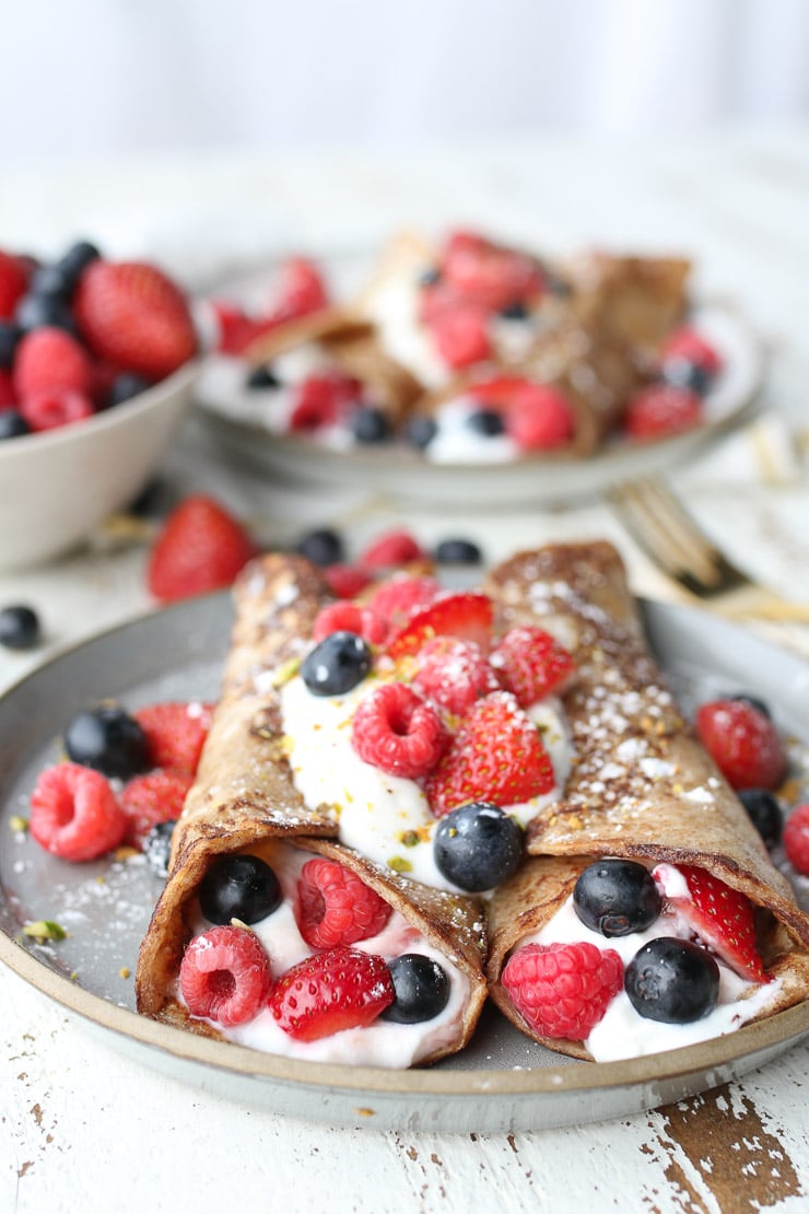 Two french toast breakfast tortilla wraps stuffed with yogurt and berries on a grey plate. 