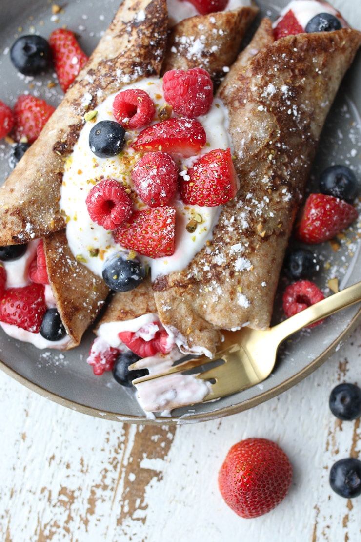 Birds eye view close up of french toast wraps on a grey plate topped with yogurt and berries.