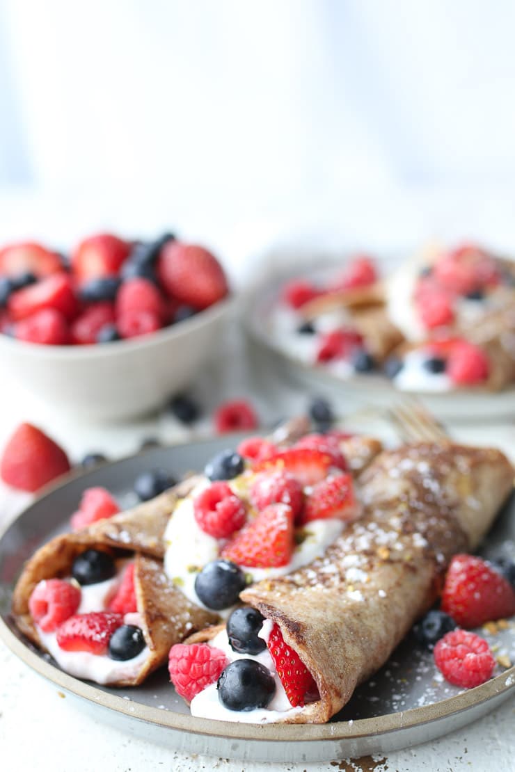 Two yogurt breakfast wraps on a grey plate topped with berries .
