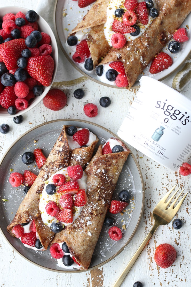 Birds eye view of two breakfast wraps stuffed with yogurt and topped with berries with a container of siggis yogurt on the side. 