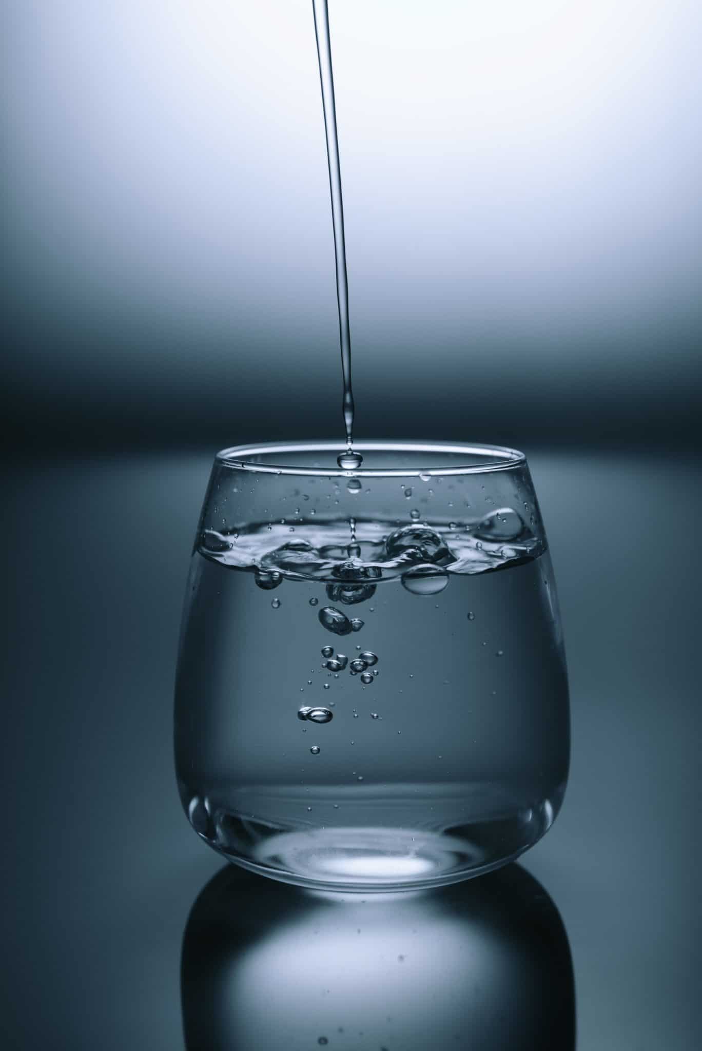 clear glass of water against a dark grey background with additional water being poured into the glass