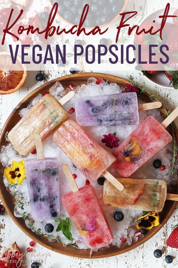 pinterest image of multiple vegan kombucha fruit popsicles for summer snacking, served over a wooden bowl full of ice garnished with fresh berries and edible flowers 