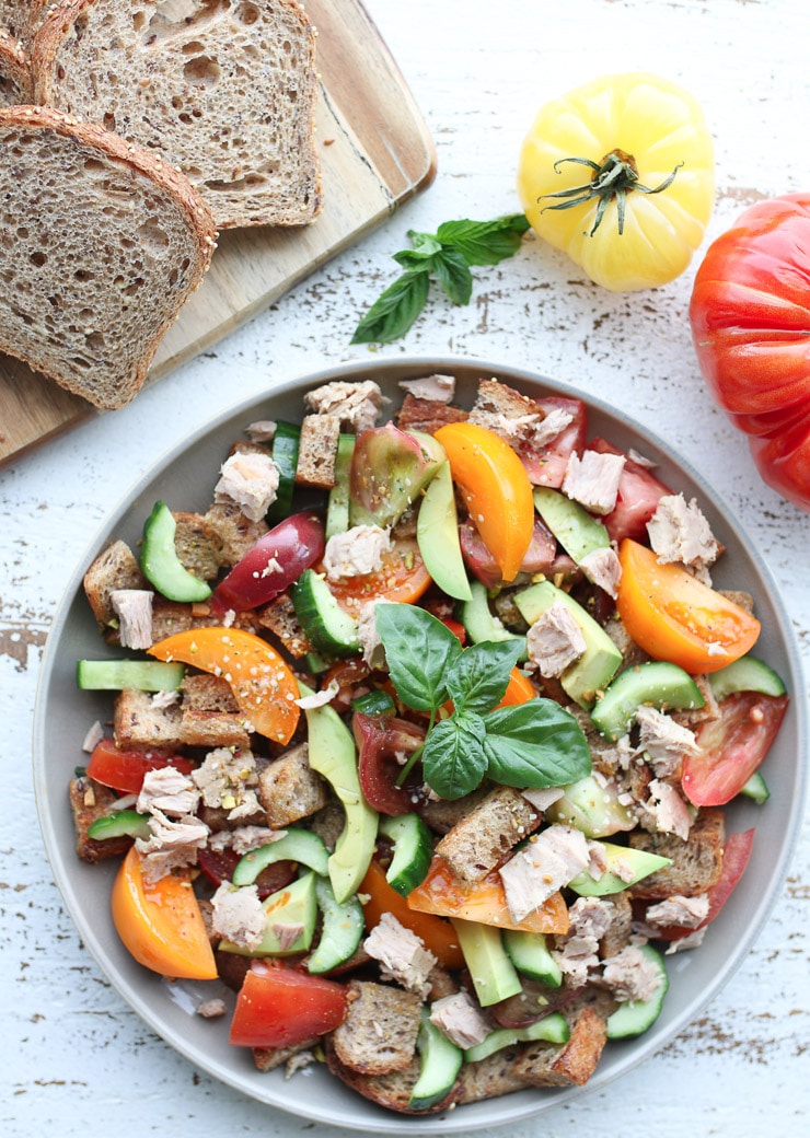 birds eye view of panzanella salad garnished with fresh basil with tomato and bread slices in the background 