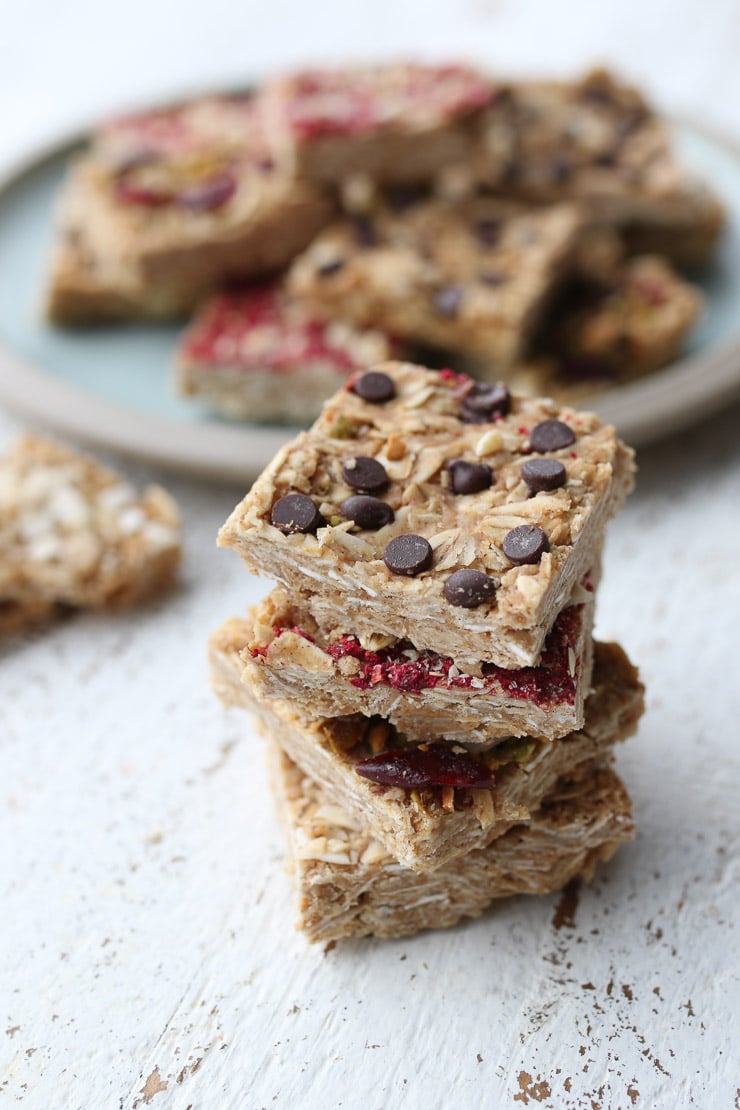 Four oatmeal bars stacked on top of one another with a plate of oat bars in the background.