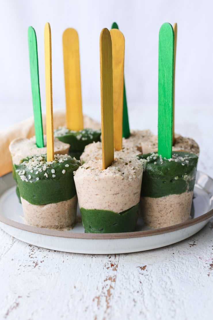several homemade veggie popsicles with yellow and green popsicles sticks standing on a white plate 