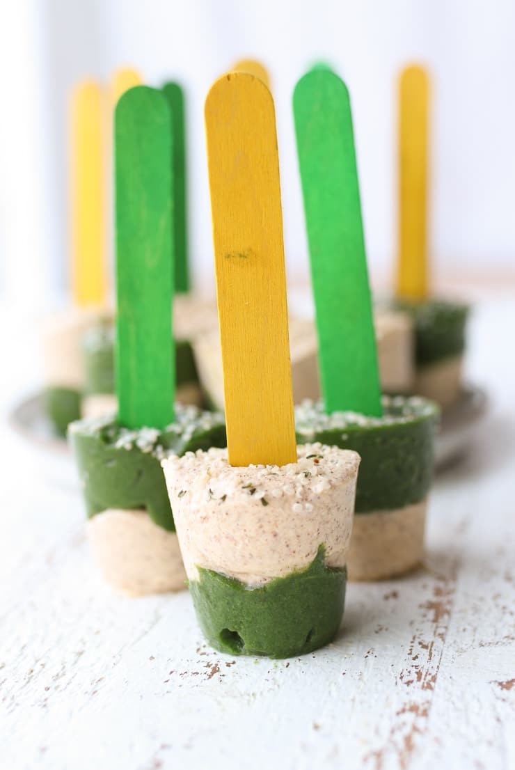 a homemade veggie popsicle with a yellow stick sprinkled with hemp seed with several veggie popsicles in the background 