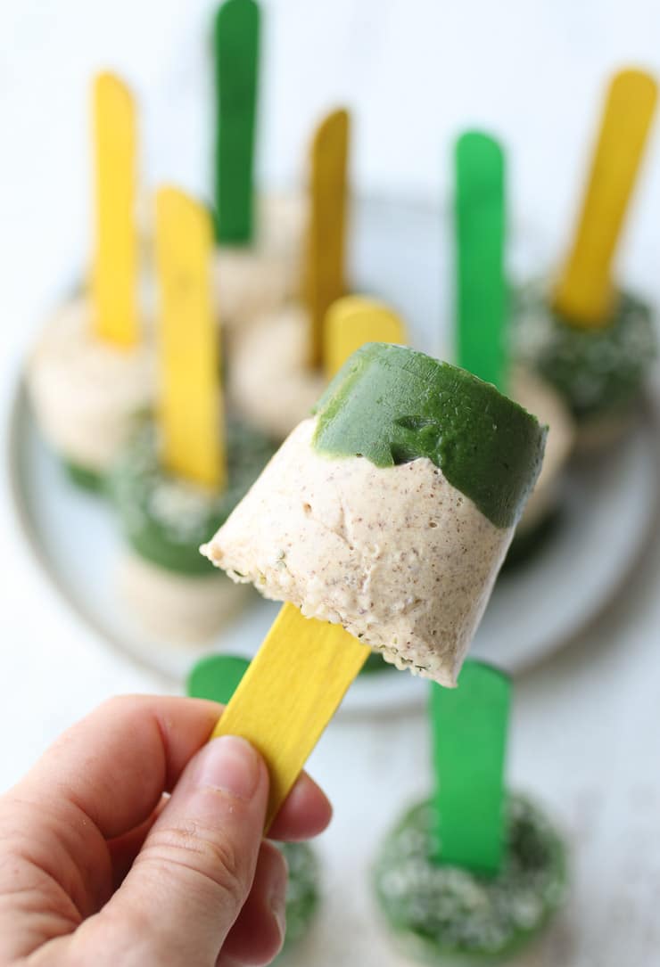 a hand holding up a vegan baby led weaning popsicle with a yellow popsicle stick 