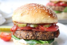 vegan black bean burger on a plate with a pickle and tomatoes