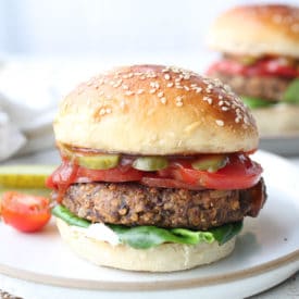 vegan black bean burger on a plate with a pickle and tomatoes