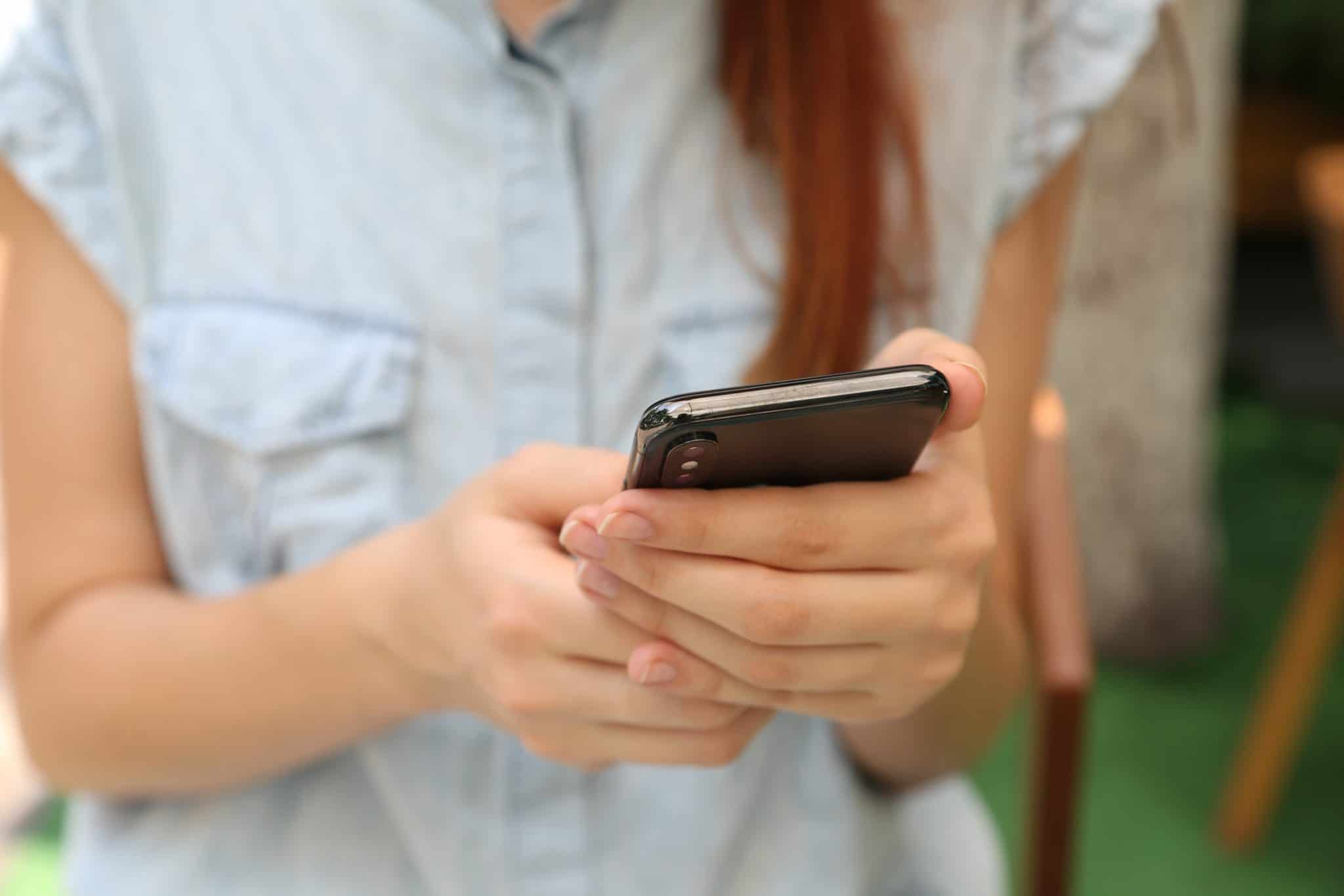 A woman wearing a blue shirt using her smart phone. 