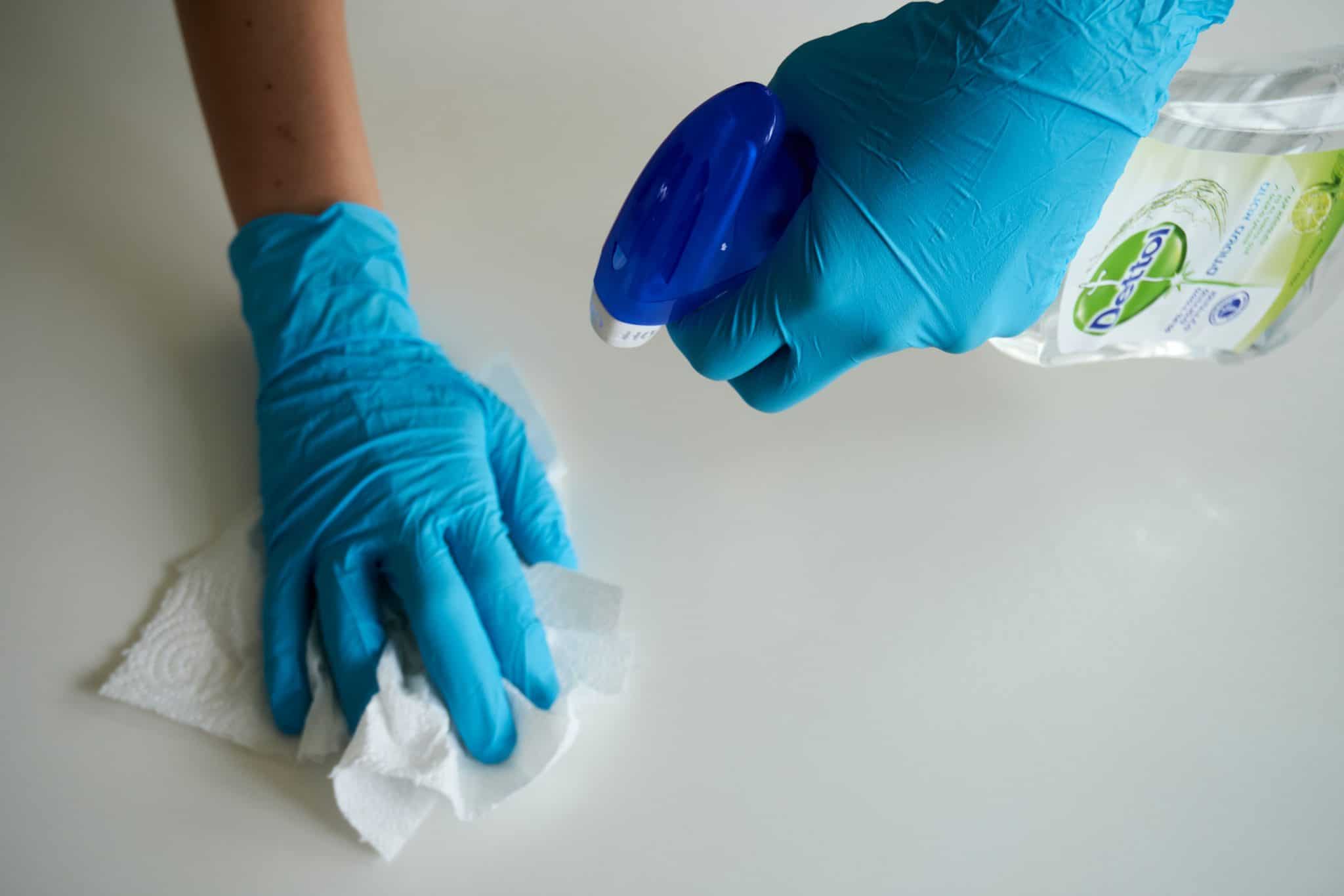 person wearing blue gloves and sanitizing a surface with paper towel 