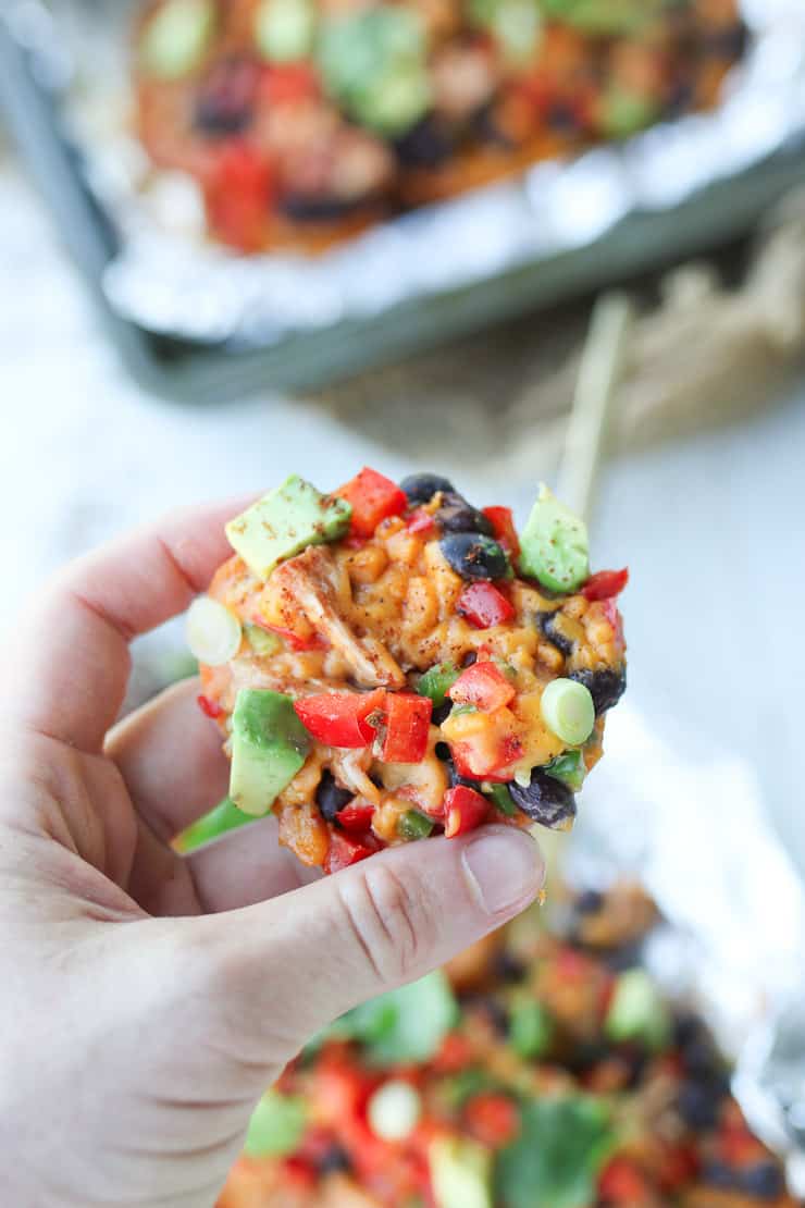 person holding up a sweet potato with nacho toppings