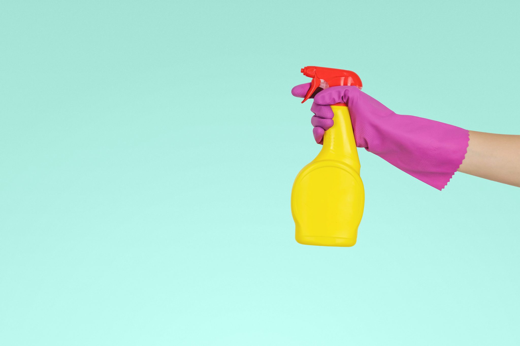 person wearing a purple glove and spraying a disinfectant in a yellow bottle 