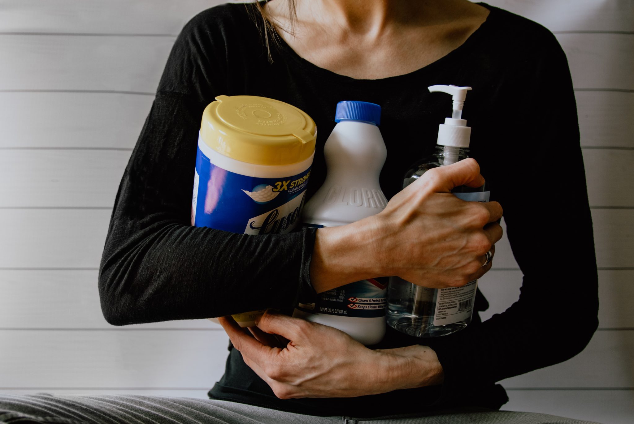 woman in black shirt holding a variety of cleaning and sanitation products 