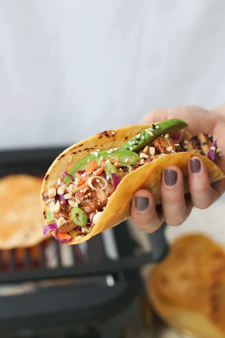 Person holding vegan tacos with peanut sauce.