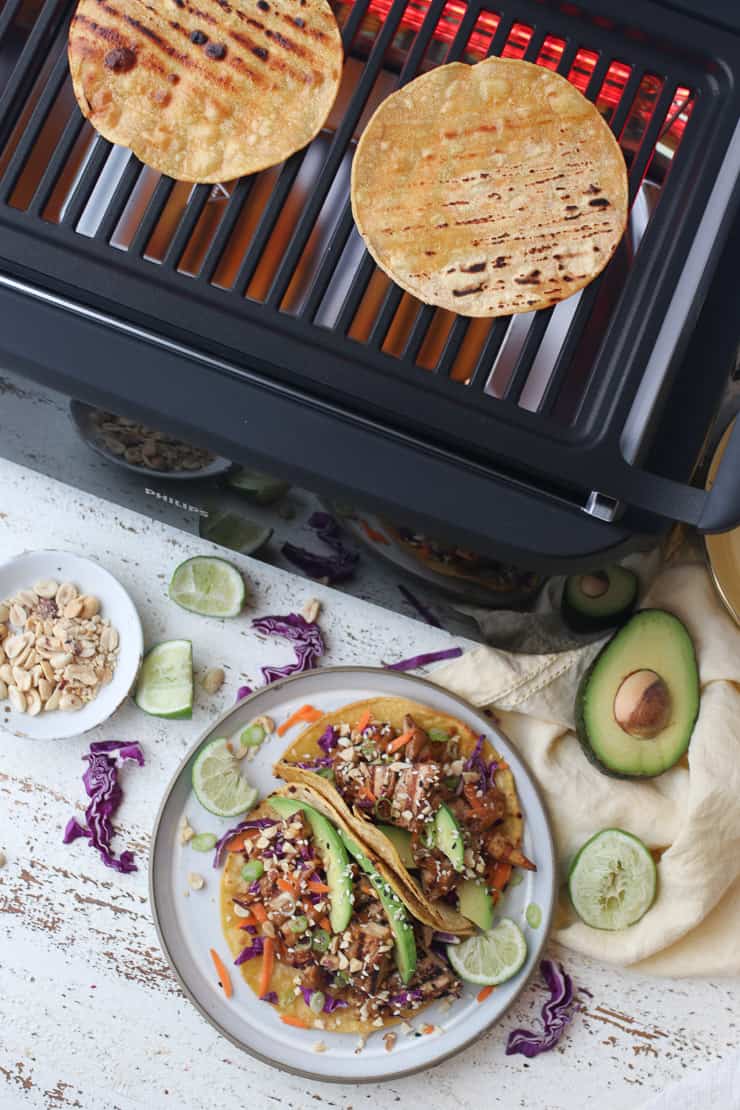 Making a tofu tacos recipe on the grill, with a plate of tofu tacos on the counter.