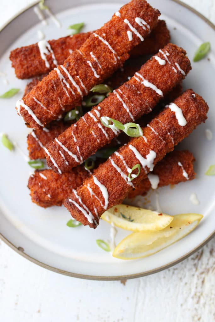 Overhead image of multiple vegan buffalo tofu sticks with sauce drizzled on top.