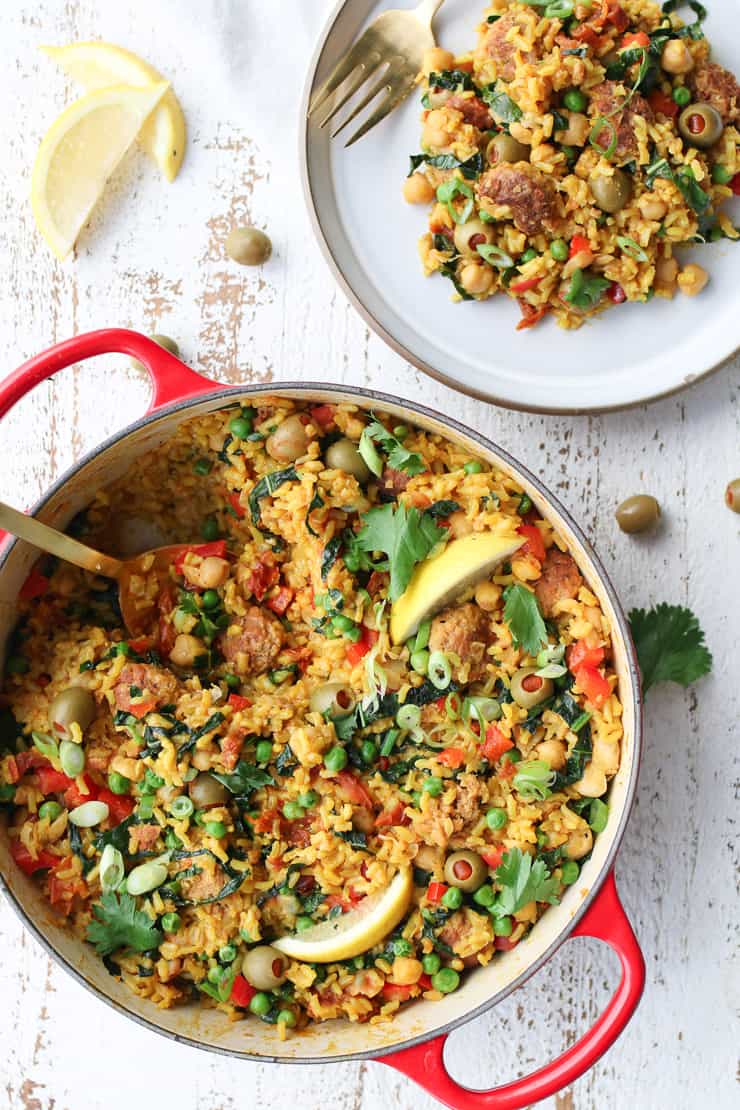 birds eye view of paella in red pan and served on a white plate garnished with two lemon wedges .