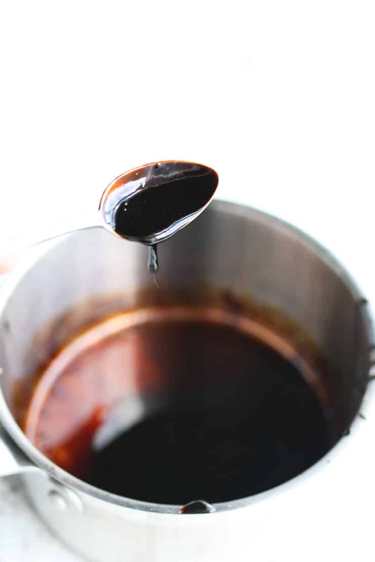 a spoon scooping up balsamic glaze from a pot 