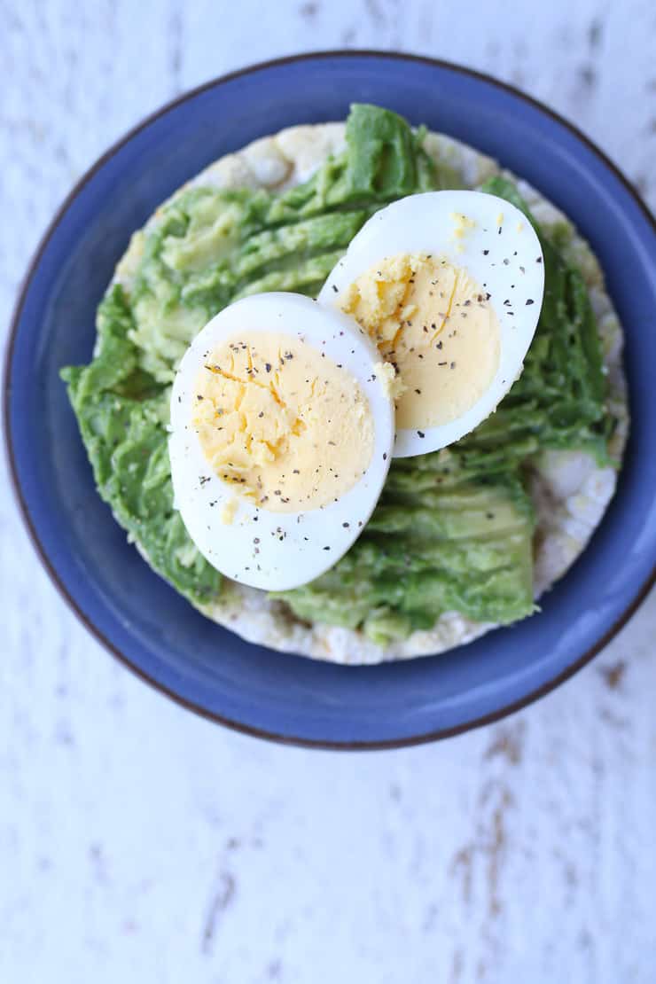 a rice cake topped with avocado and a boiled egg on a blue plate 