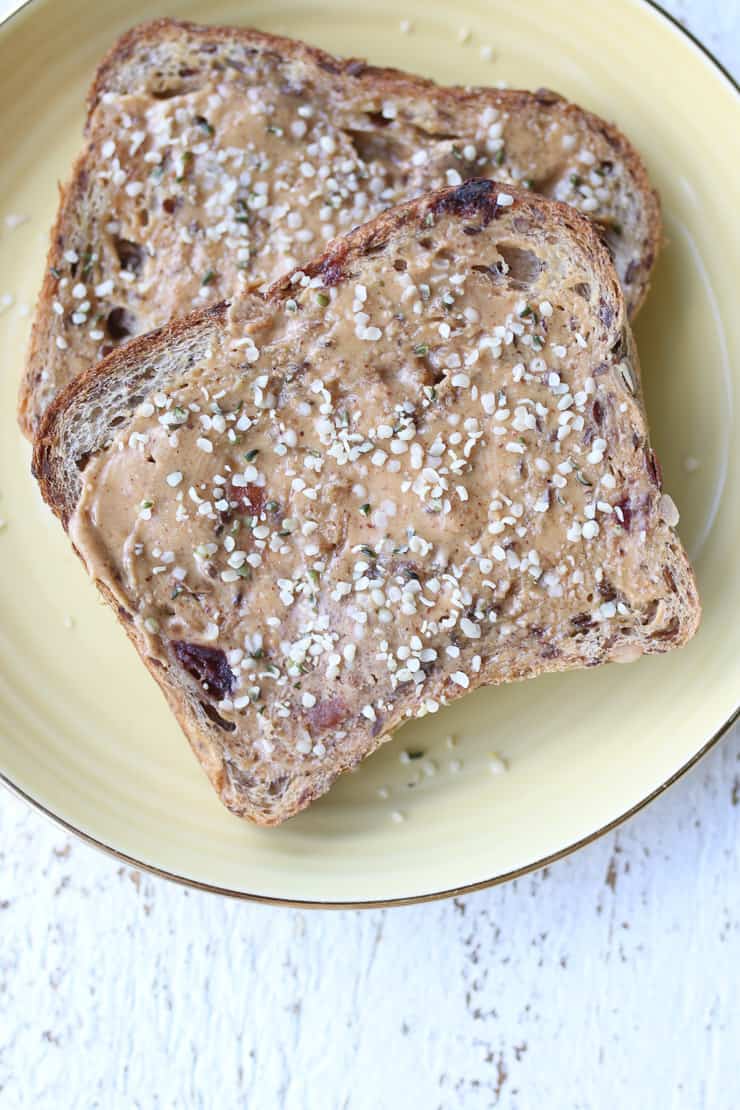 two pieces of toast with nut butter and hemp seed on a yellow plate 