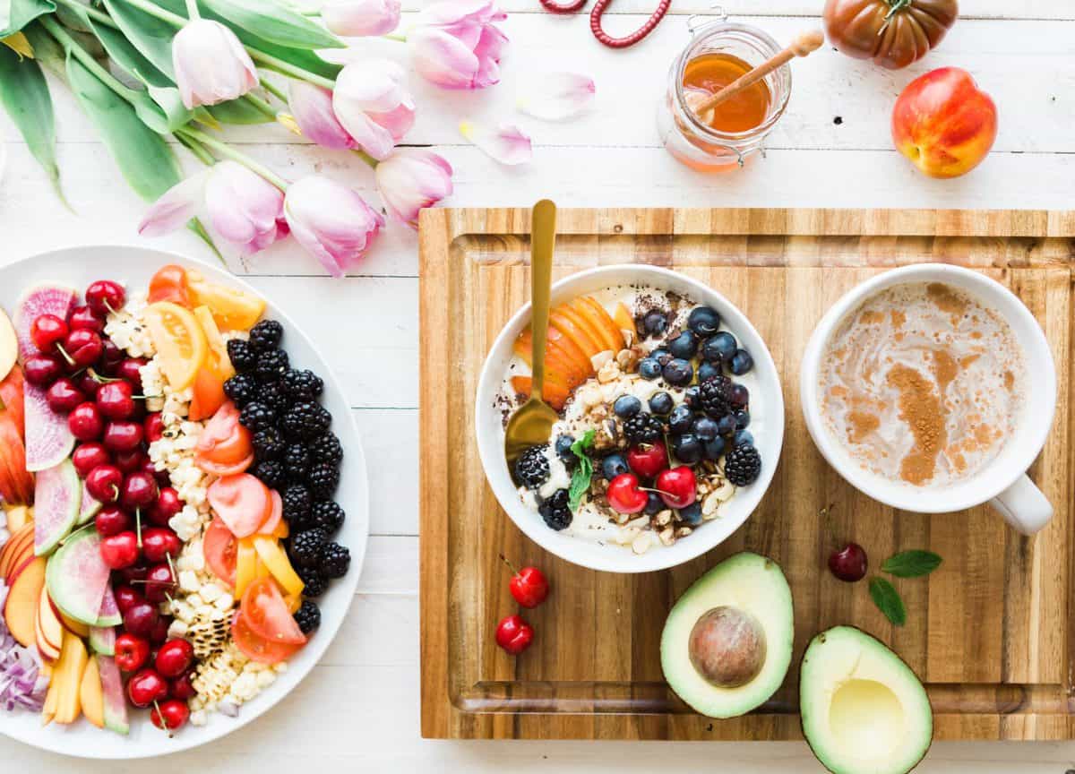 A plate of fruit and vegetables, bowl of oatmeal with fruit, and cup of coffee.