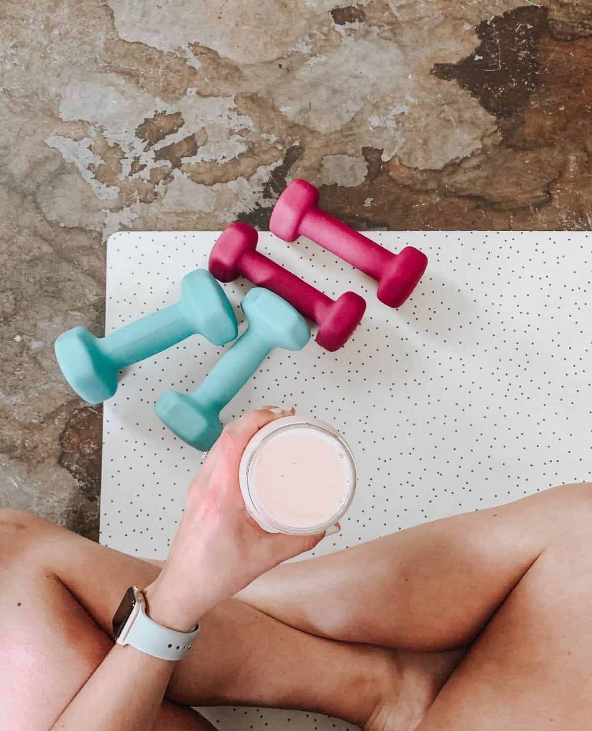 Person sitting on a yoga matt drinking a smoothie.