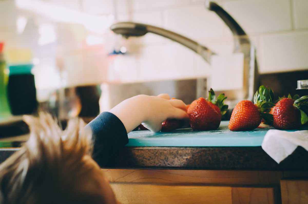 child reaching for strawberries over a kitchen counter