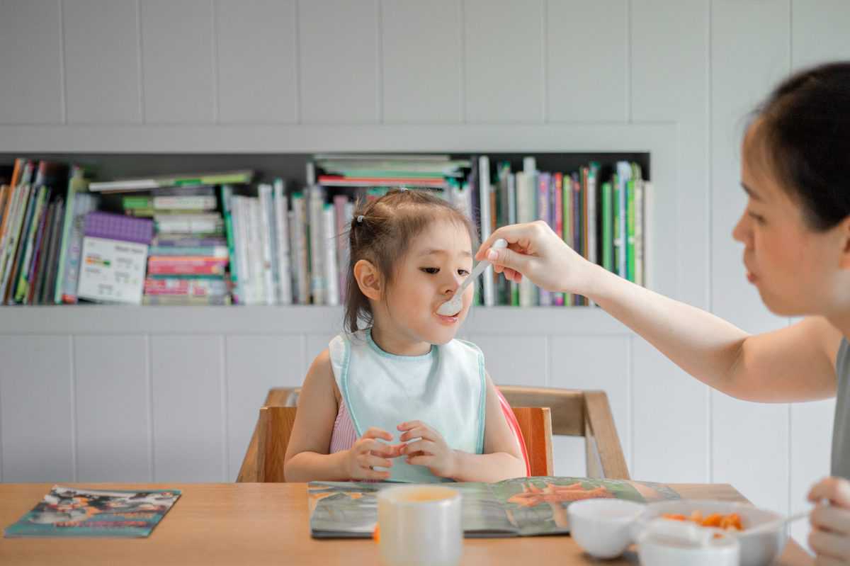 a toddler getting spoonfed by their mother 