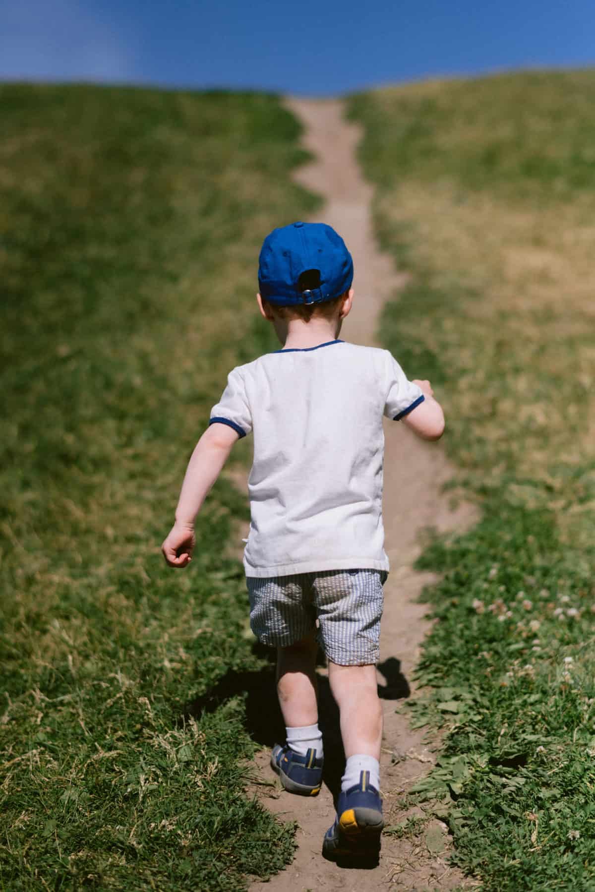 baby E wearing a blue hat running up a hill 