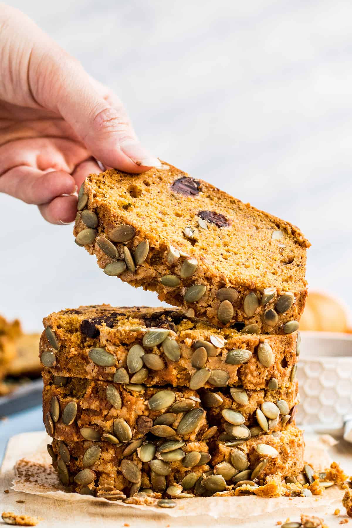 A hand picking up a piece of vegan pumpkin bread from a stack of four pieces of pumpkin bread on parchment paper. 