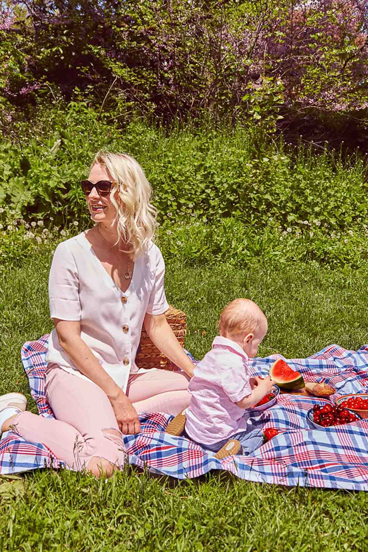 Abbey and Baby I sitting outside on a picnic blanket surrounded by red fruit.