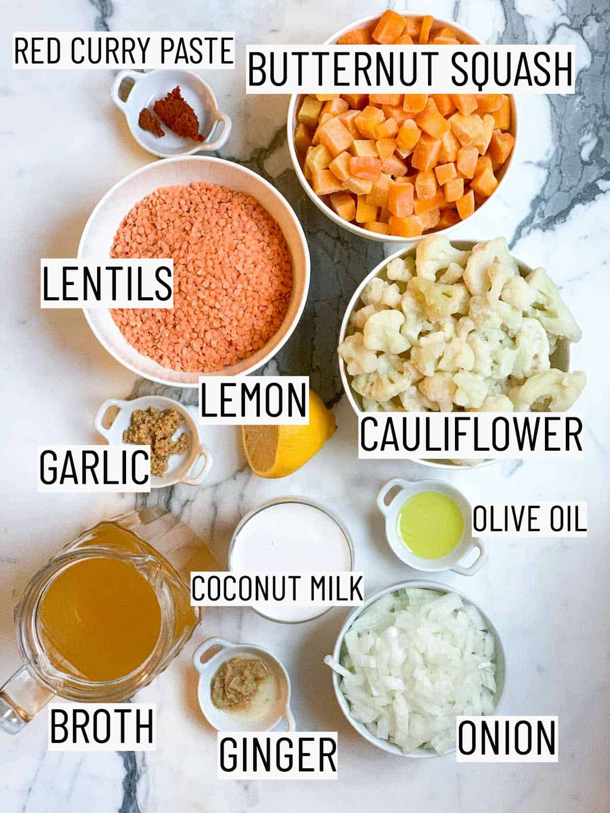 flatlay of ingredients required to make the soup: red curry paste, butternut squash, cauliflower, olive oil, lemon, lentils, garlic, coconut milk, onion, ginger, and broth.